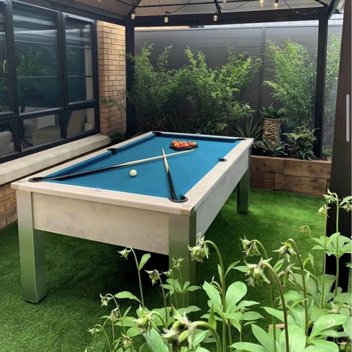 Outdoor pool table with blue cloth in a garden room surrounded by plants