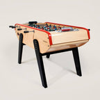 Bonzini B90 football table in natural beech with red rails and black legs, three-quarter view