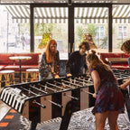 Group of friends playing on a Bonzini giant football table in a bright venue