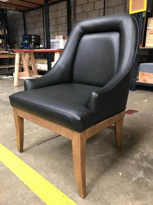 Black leather poker chair with curved arms on a natural wood frame
