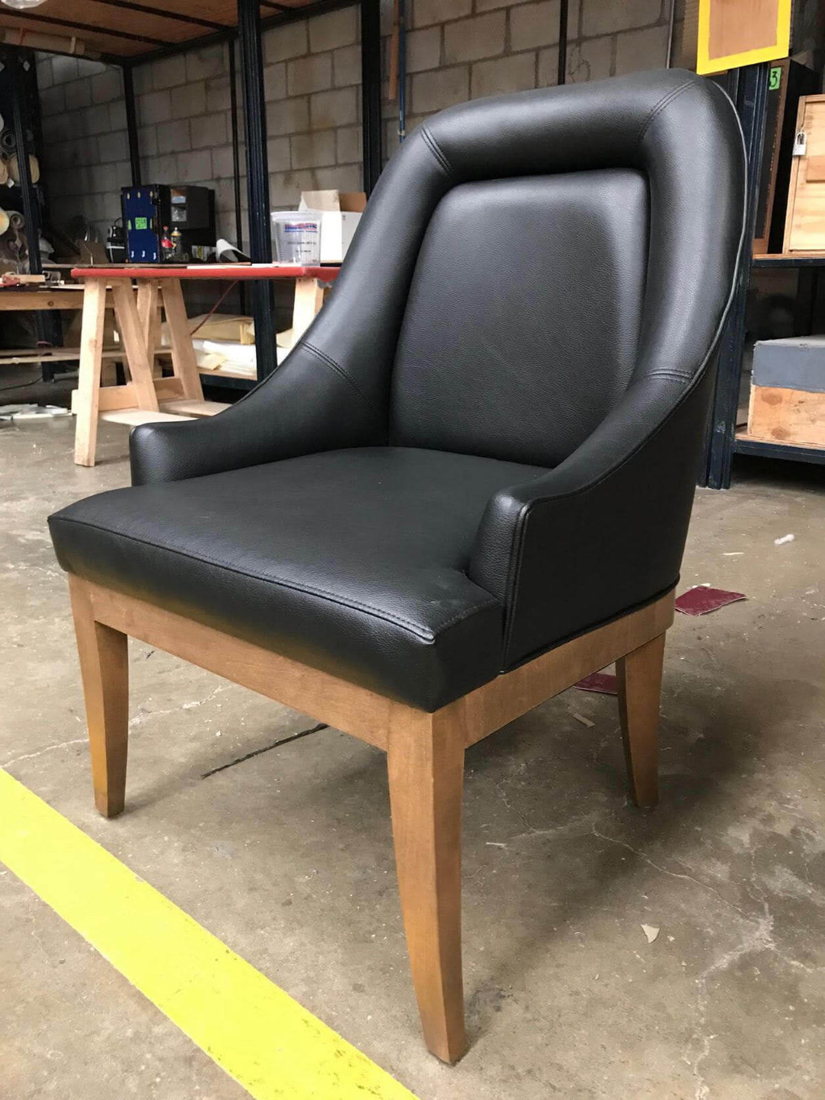 Black leather poker chair with curved arms on a natural wood frame