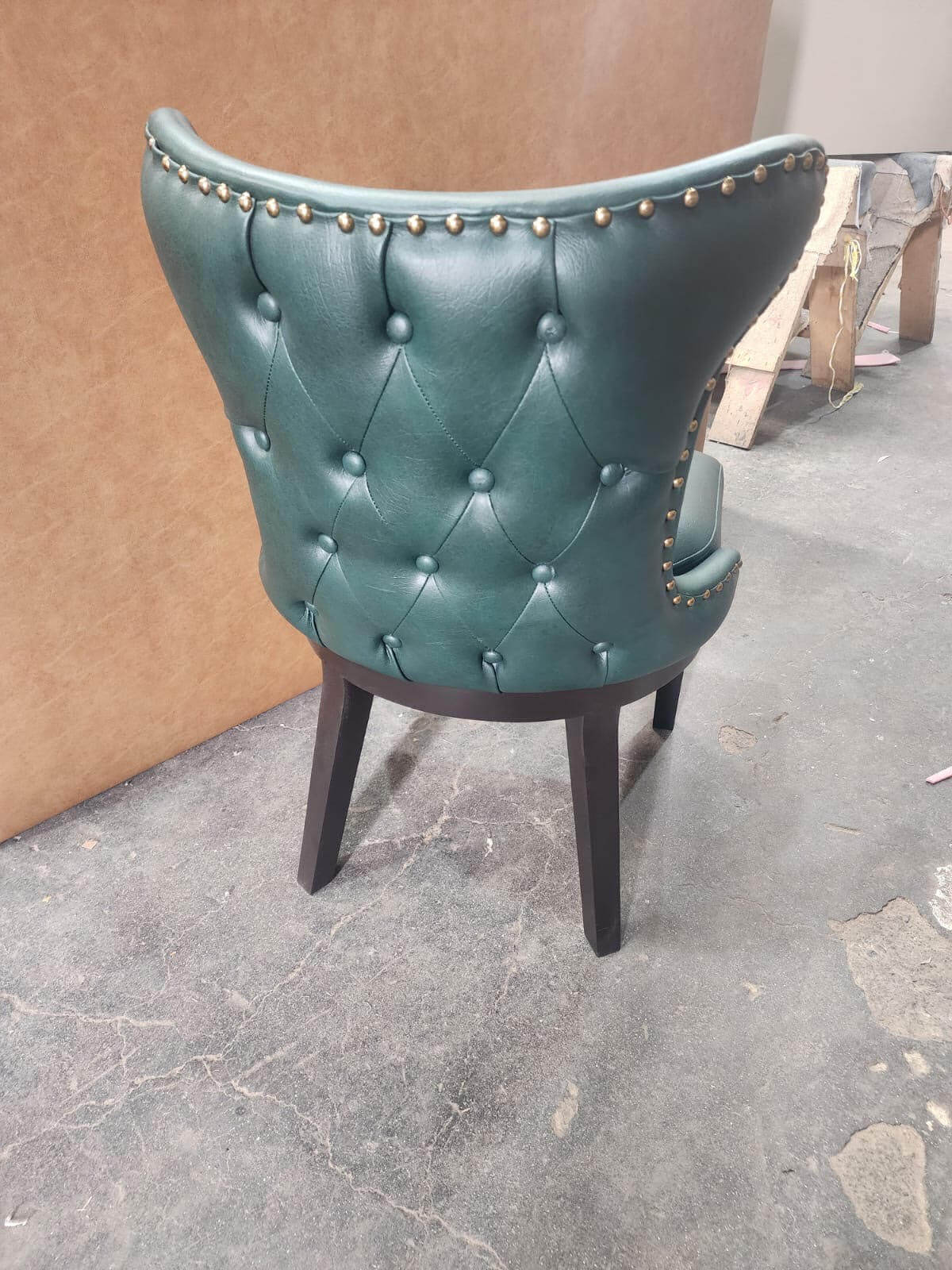 Back of a green button-tufted leather poker chair with stud trim and dark wood legs