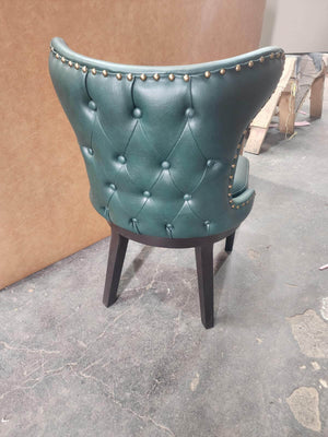 Back of a green button-tufted leather poker chair with stud trim and dark wood legs