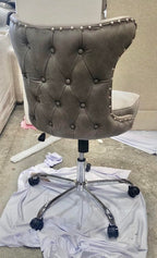 Back of a grey button-tufted leather poker chair with stud trim on a chrome swivel base with castors