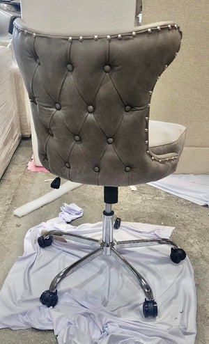 Back of a grey button-tufted leather poker chair with stud trim on a chrome swivel base with castors