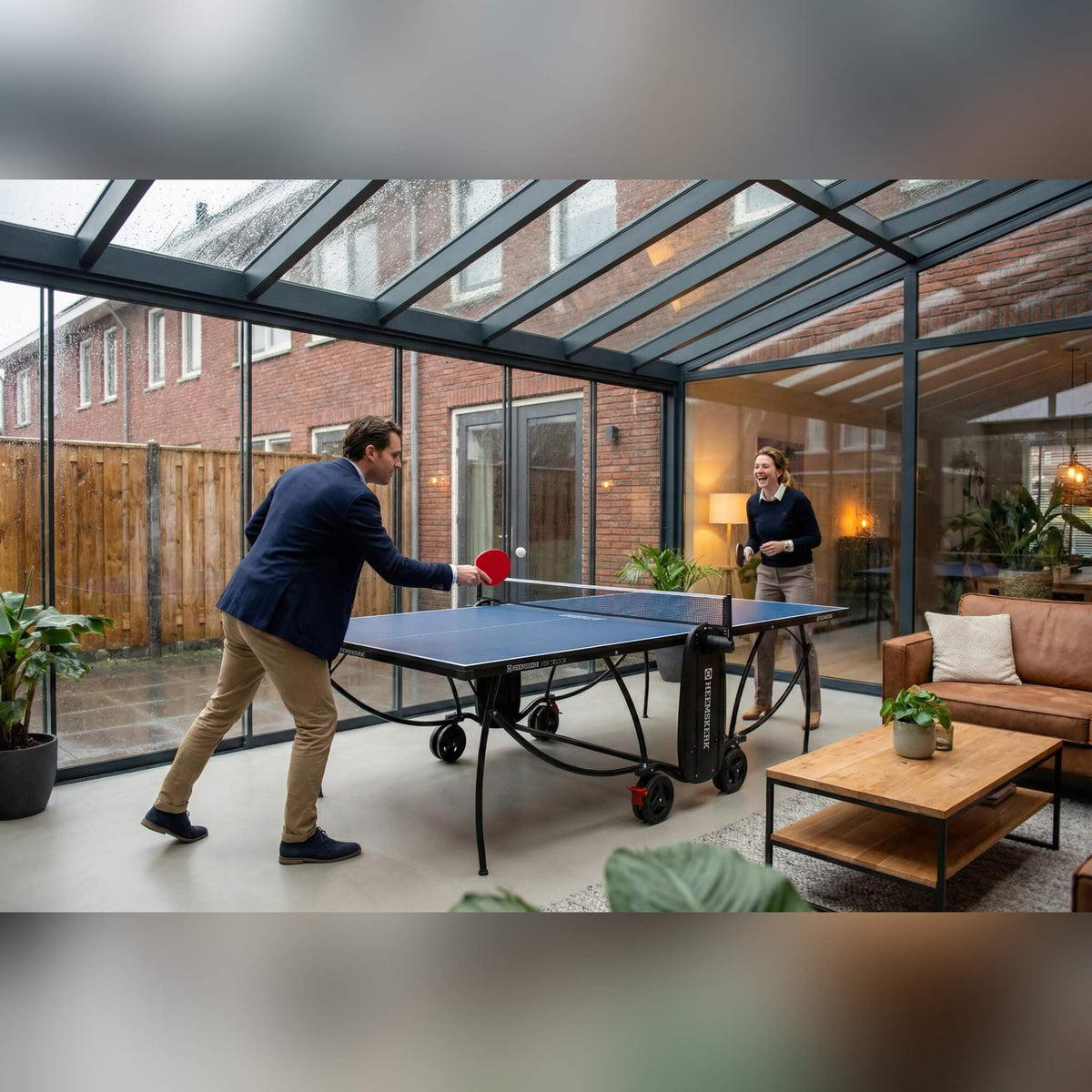 Two people playing on a blue Heemskerk 1850 indoor table tennis table in a conservatory