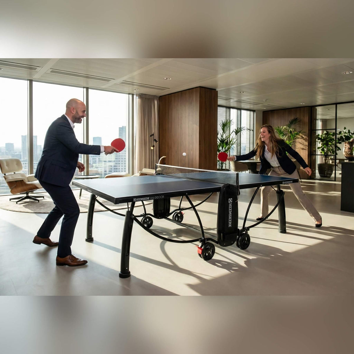 Two colleagues playing on a blue Heemskerk 2250 indoor table tennis table in an office