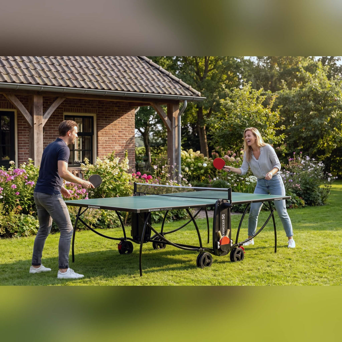 Couple playing on a green Heemskerk 1900 outdoor table tennis table in a garden