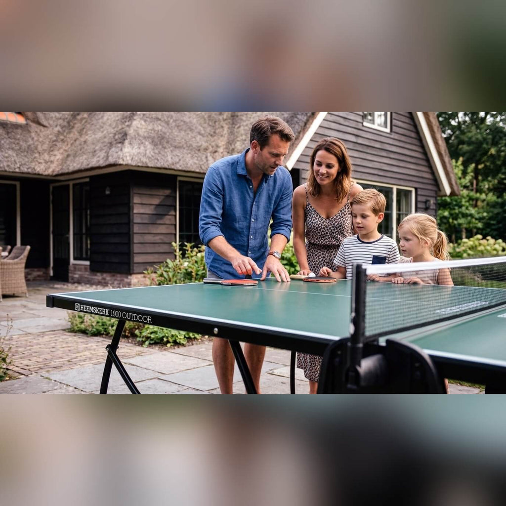 Family playing on a green Heemskerk 1900 outdoor table tennis table on a patio