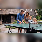 Family playing on a green Heemskerk 1900 outdoor table tennis table on a patio
