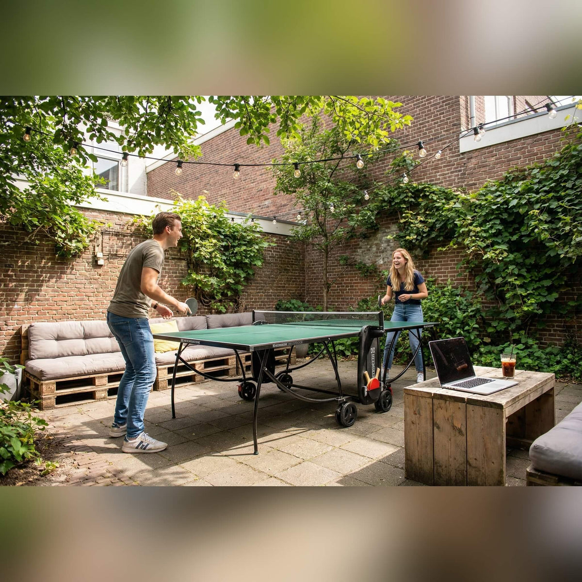 Two people playing on a green Heemskerk 1900 outdoor table tennis table in a courtyard garden