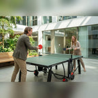 Two people playing on a green Heemskerk 2300 outdoor table tennis table in an office courtyard