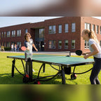 Two girls playing on a green Heemskerk 2300 outdoor table tennis table on a school lawn
