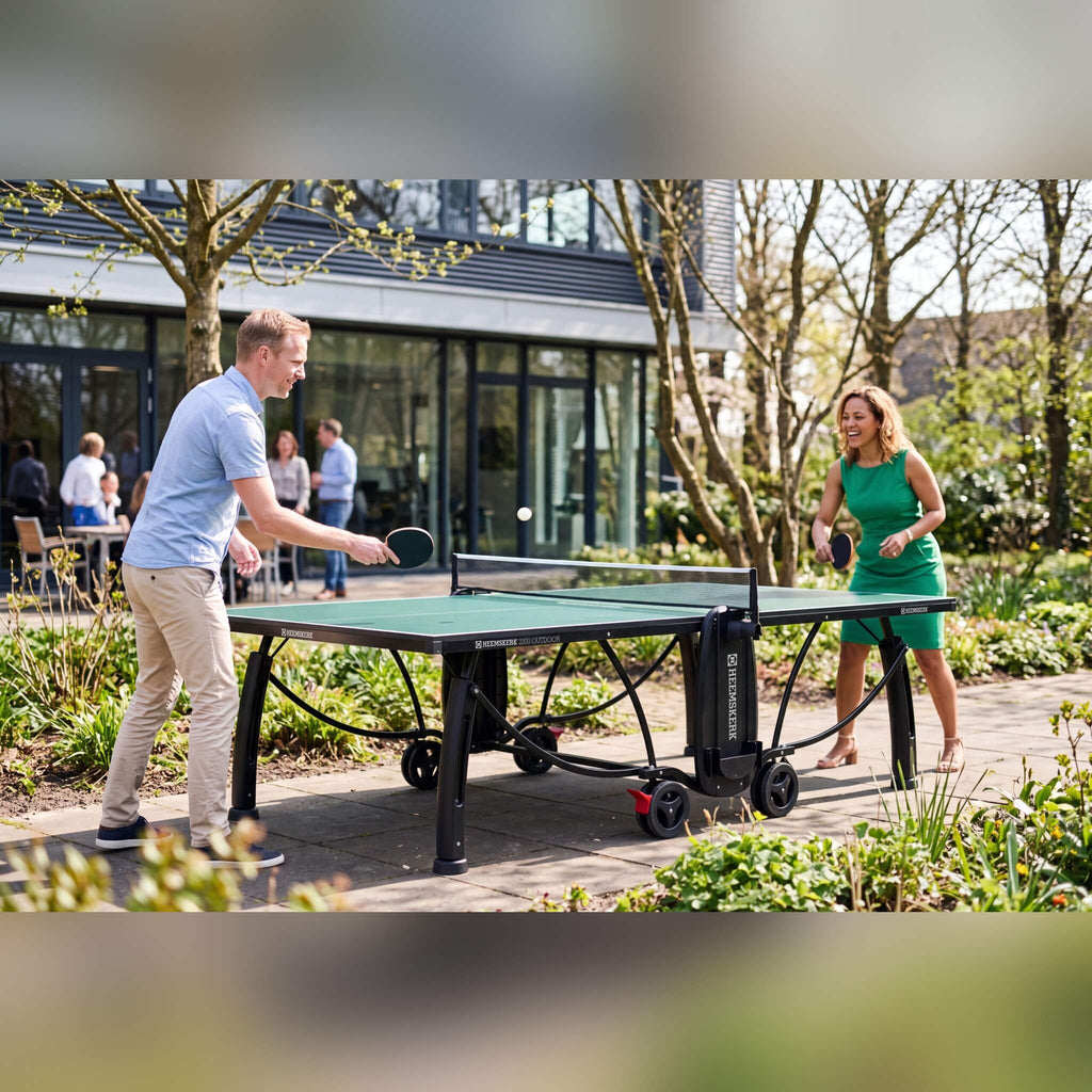 Two people playing on a green Heemskerk 2300 outdoor table tennis table in an office garden