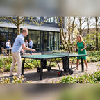 Two people playing on a green Heemskerk 2300 outdoor table tennis table in an office garden