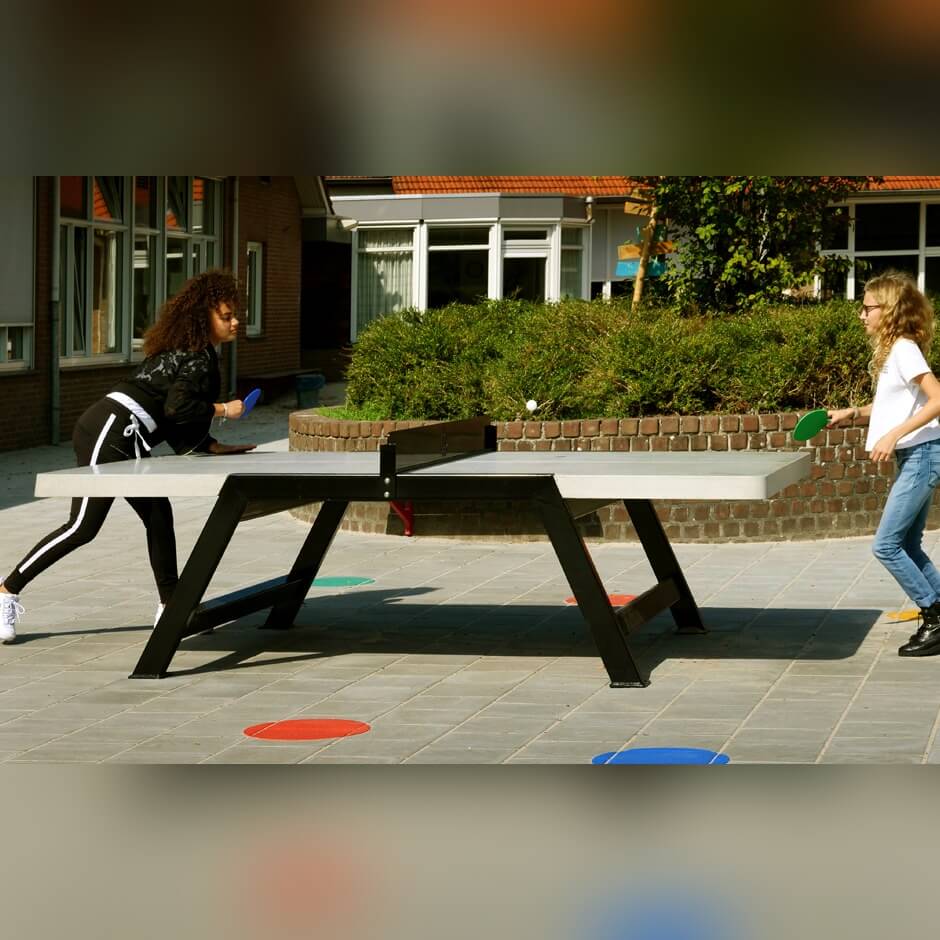 Two girls playing on a Heemskerk Beta concrete outdoor table tennis table in a schoolyard