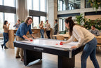 Two people playing on the Heemskerk Coliseum air hockey table in a busy canteen
