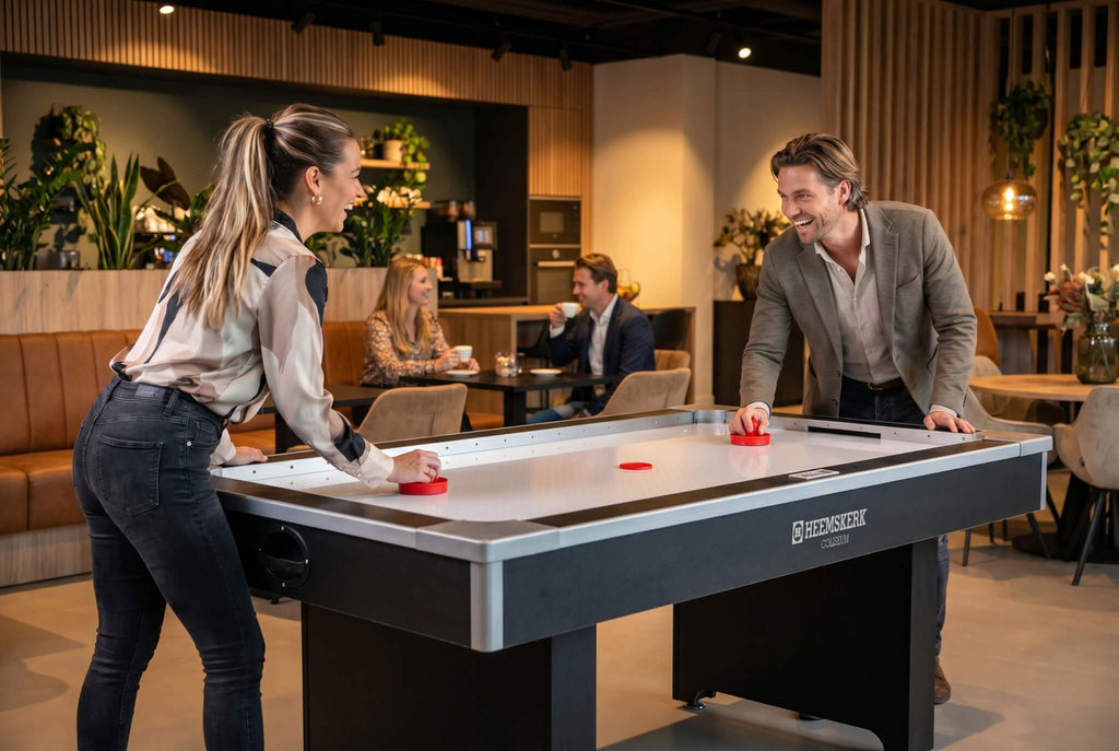 Two colleagues playing on the Heemskerk Coliseum air hockey table in an office lounge