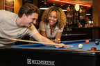 Couple laughing as they line up a shot on a Heemskerk Dallas pool table in a bar