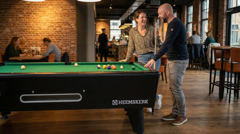 Two people playing pool on a Kick Shot table with green cloth in a busy bar