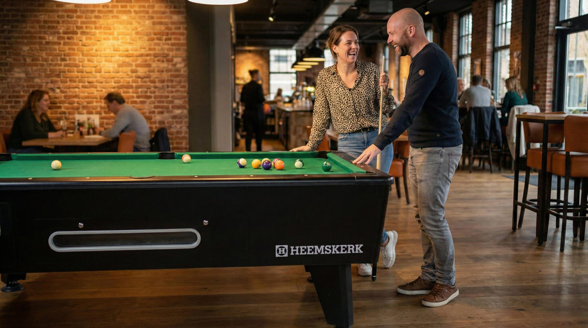 Two people playing pool on a Kick Shot table with green cloth in a busy bar