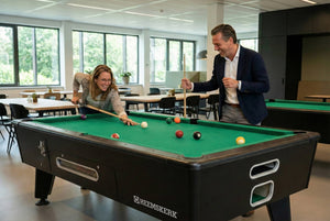 Two colleagues playing on a Kick Shot pool table with green cloth in a staff canteen