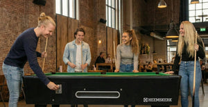 Group of friends paying for a game at the side of a Kick Shot pool table in a bar