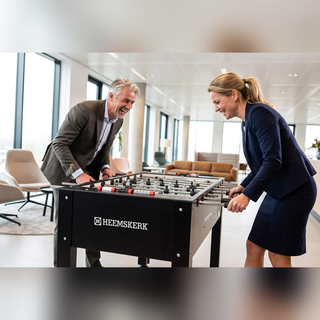 Two colleagues laughing over a game on a Heemskerk King Pro foosball table in an office