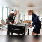 Two colleagues laughing over a game on a Heemskerk King Pro foosball table in an office