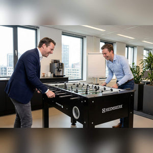Two men playing on a Heemskerk King Pro foosball table in an open-plan office