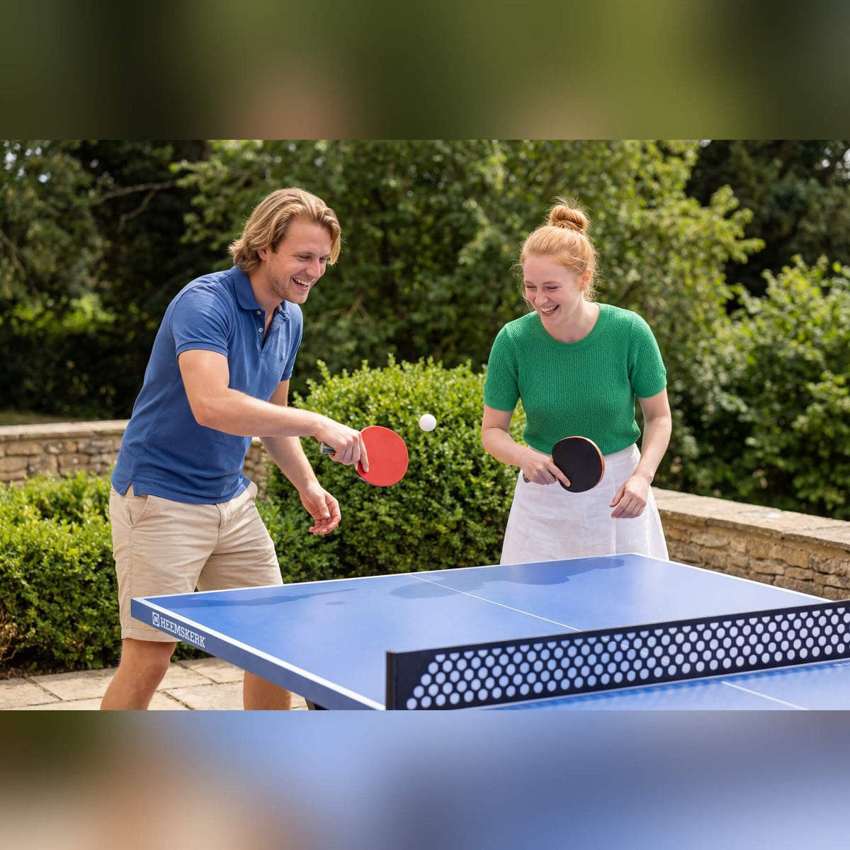 Two people playing on a Heemskerk Lima outdoor table tennis table in a garden