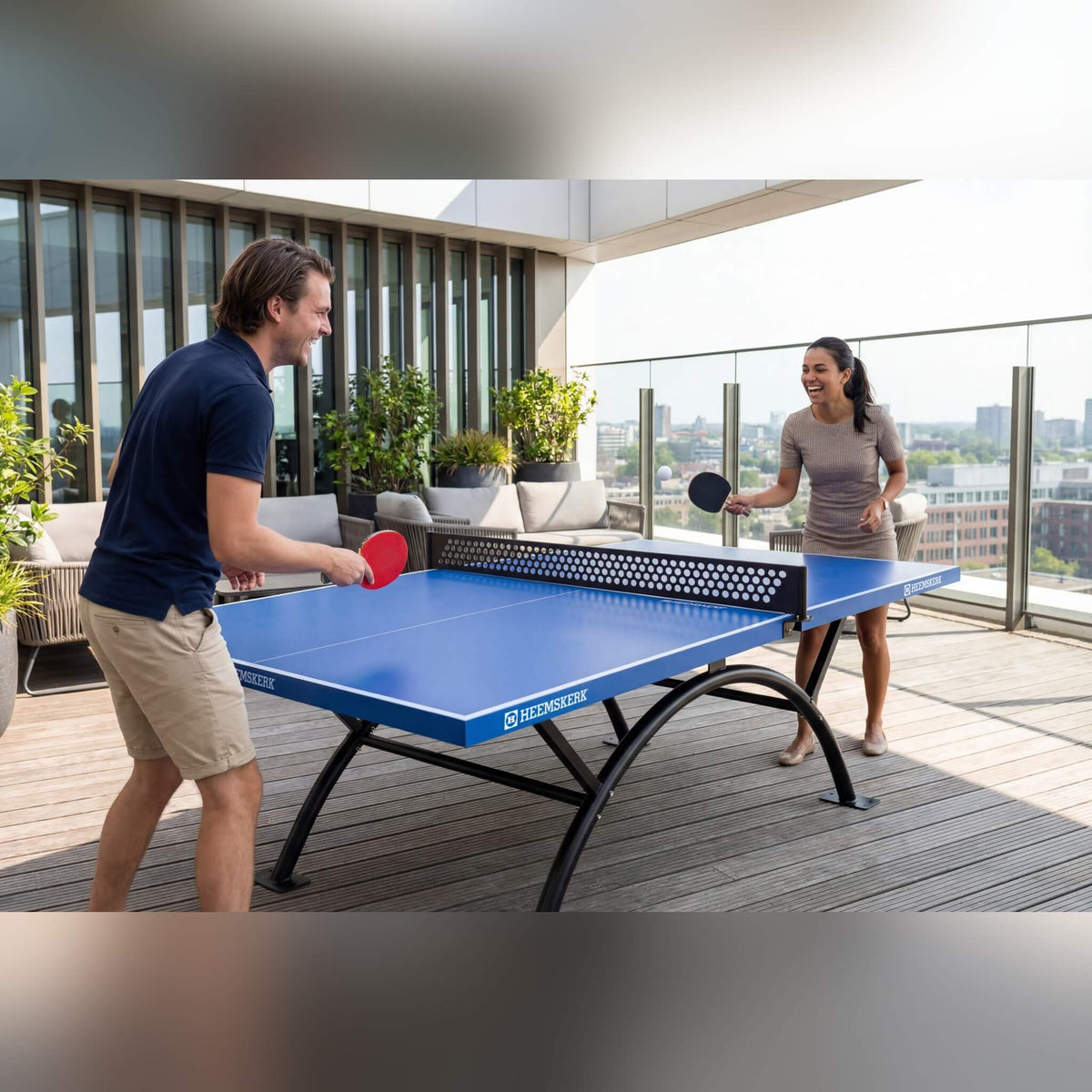 Couple playing on a Heemskerk Lima outdoor table tennis table on a rooftop terrace