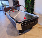 Heemskerk Navona air hockey table with a red pusher on the metal playfield in a lounge with a plant wall