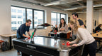 Colleagues playing a game on the Heemskerk Navona air hockey table in an open-plan office