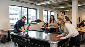 Colleagues playing a game on the Heemskerk Navona air hockey table in an open-plan office