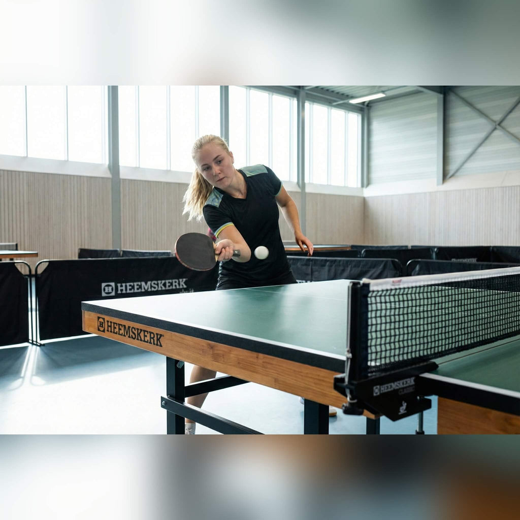 Player serving on a green Heemskerk Novi 2400 table tennis table in a sports hall
