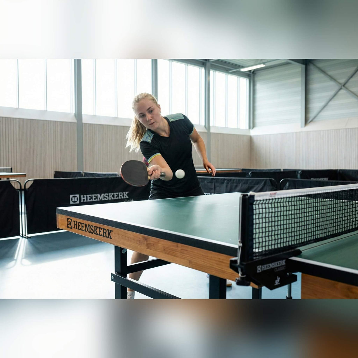 Player serving on a green Heemskerk Novi 2400 table tennis table in a sports hall