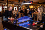 Two friends playing on the Heemskerk Parthenon air hockey table in a busy bar