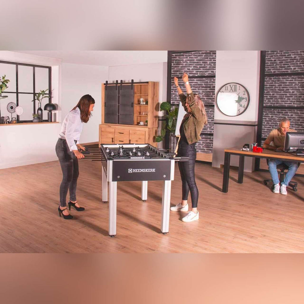 Two women playing on a Heemskerk Soccer School football table in an office