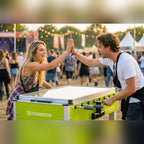 Two friends high-fiving over a Heemskerk Sunshine outdoor football table at a festival