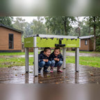 Two children sheltering under a Heemskerk Sunshine outdoor football table on a wet deck
