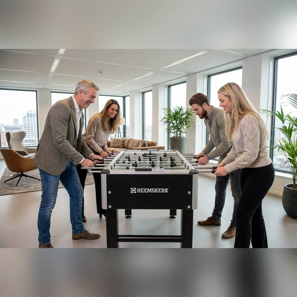 Four colleagues playing on a Heemskerk TacTic football table in an office