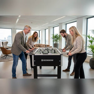 Four colleagues playing on a Heemskerk TacTic football table in an office