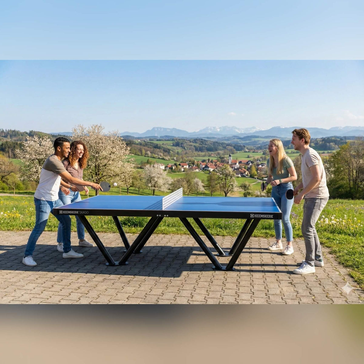 Four people playing doubles on a Heemskerk Tango outdoor table tennis table on a terrace