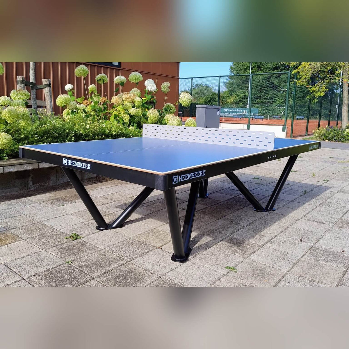 Heemskerk Tango outdoor table tennis table installed on paving next to a sports court