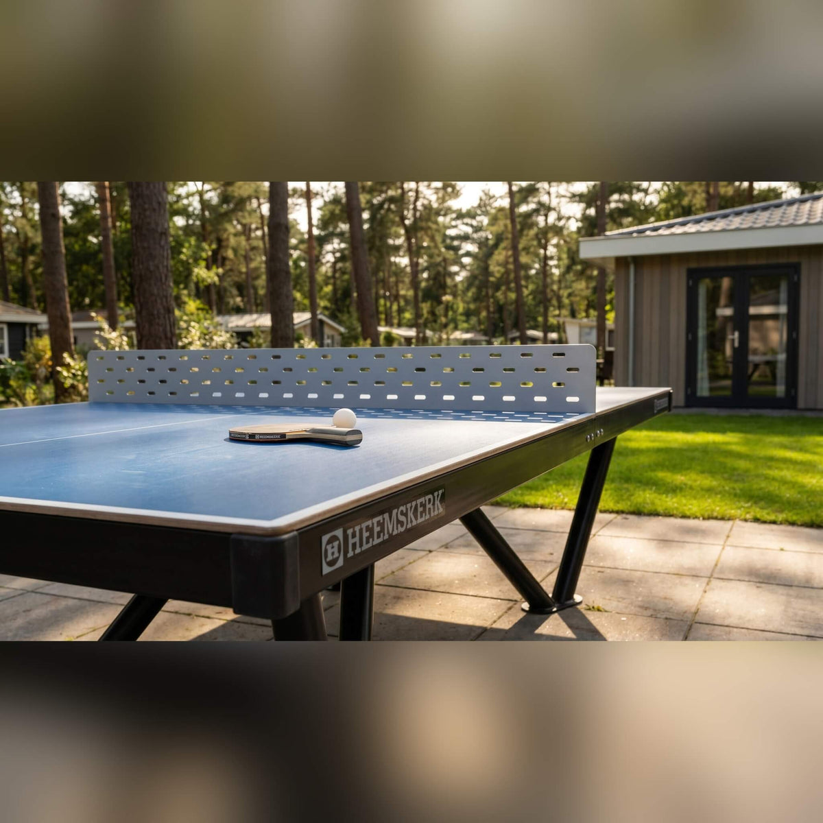Bat and ball on a Heemskerk Tango outdoor table tennis table next to a cabin