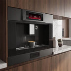 Kaiser La Perle Noire built-in coffee machine fitted into wooden kitchen units, with a cup of coffee on the drip tray