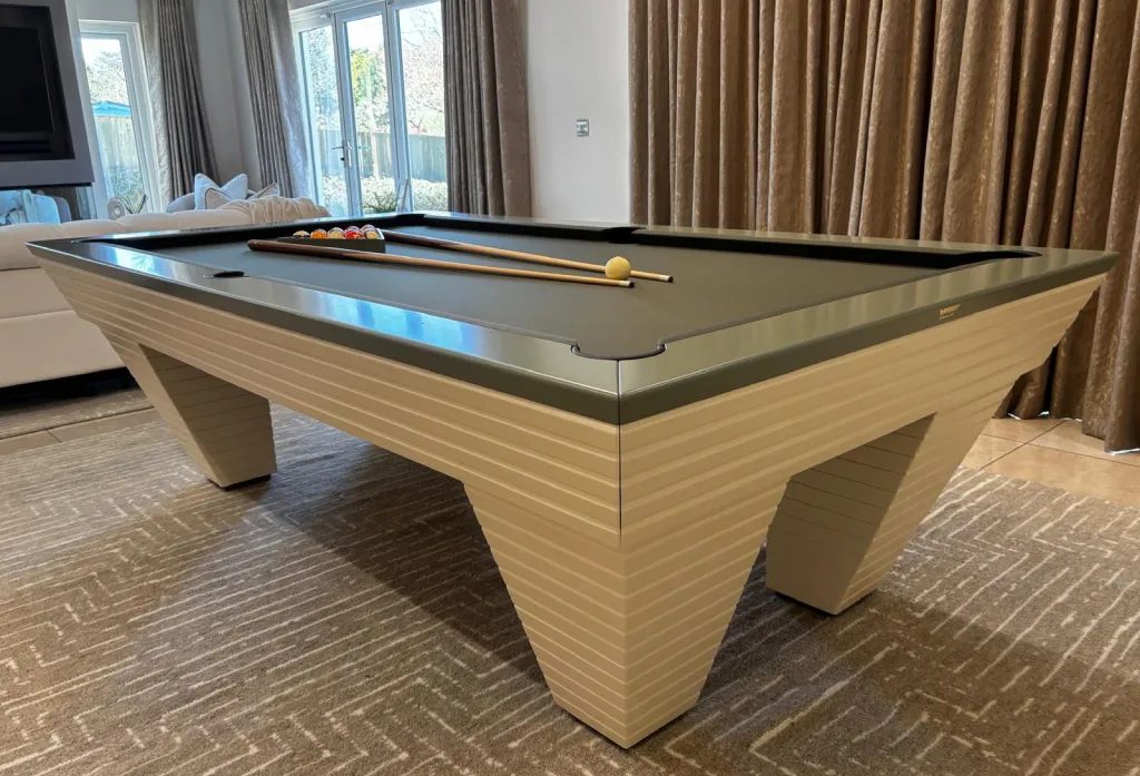 Luxury Newde pool table with ivory ribbed tilted legs, sage grey top rail and dark cloth in a living room