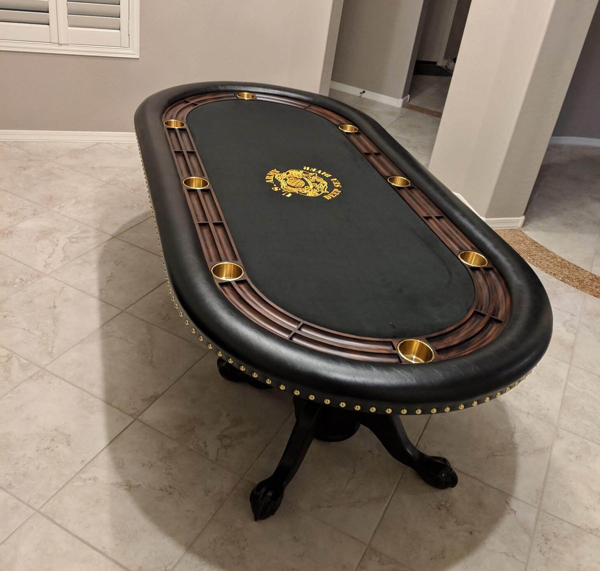 Luxury oval poker table with black cloth and gold logo, black leather rail, hardwood racetrack and brass cupholders