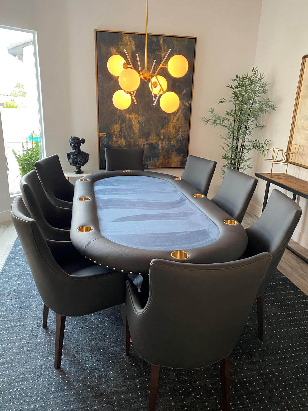 Luxury oval poker table with blue cloth, black leather rail and brass cupholders, set with leather chairs
